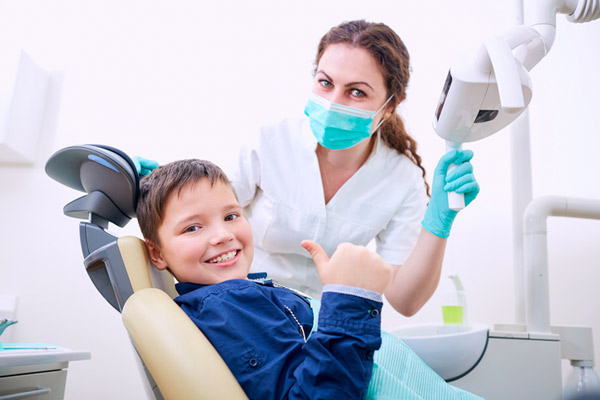 Child sitting in dental chair with doctor and giving a thumbs up