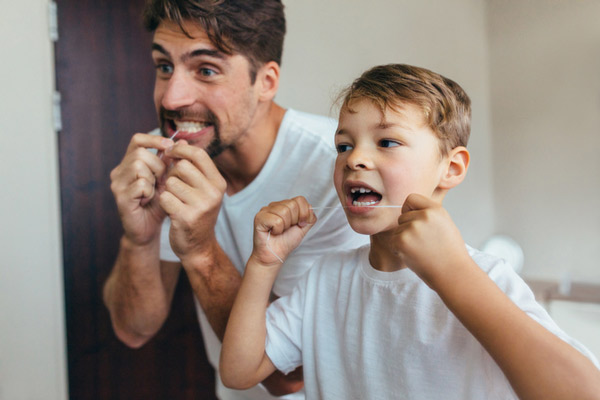 Young boy and father flossing teeth next to each other in bathroom
